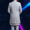 A man wearing a grey embroidered indo-western sherwani set, with a long jacket over a kurta and pants, standing against a dark background with blue and pink light streaks.