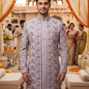 A man wearing a lavender floral embroidered sherwani with a mandarin collar, standing in a traditional wedding setting decorated with marigold garlands.