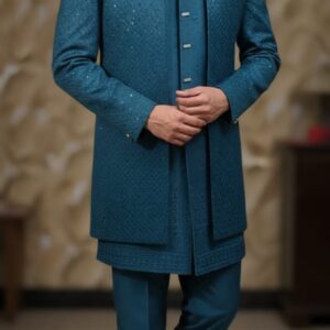 A man wearing a teal blue Indo-Western suit with a long jacket and matching pants, standing indoors.