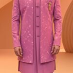 A man wearing a pink embroidered Indo-Western sherwani with a brooch and matching pants.