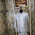 “White embroidered Jodhpuri suit with intricate pastel patterns displayed on a mannequin at Fenzi Designer Studio.”